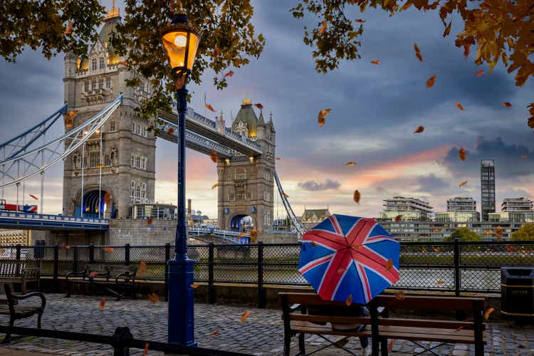 London in autumn time concept with a person holding a british umbrella sitting in front of Tower Bridge