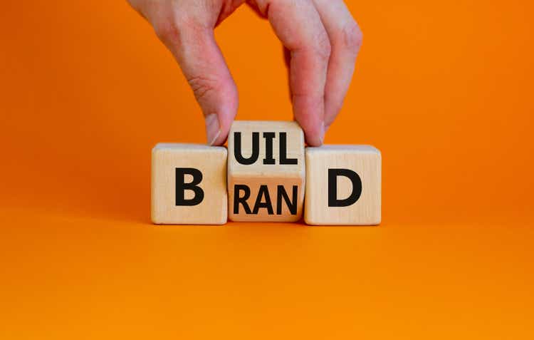 Build your brand symbol. Businessman turns wooden cubes and changes the word "build" to "brand". Beautiful orange background. Build your brand and business concept. Copy space.