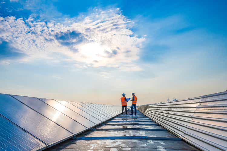 Two technicians in distance discussing between long rows of photovoltaic panels