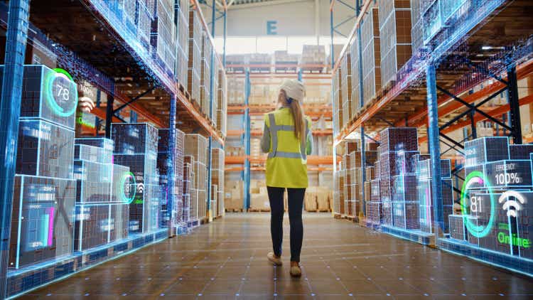 Futuristic technology retail warehouse: workers doing inventory walk as digitization process analyzes goods, cardboard boxes, logistics and products with delivery infographics in distribution center