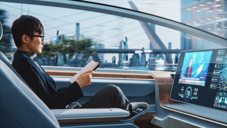 A futuristic concept: a stylish and handsome Japanese businessman wearing notebook reading glasses and watching news on an augmented reality screen while sitting in a zero-emissions self-driving car.