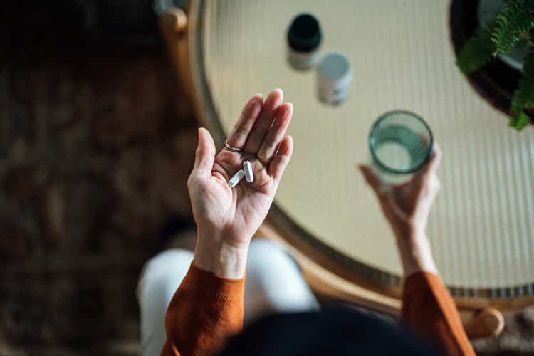 Overhead view of senior Asian woman feeling sick, taking medicines in hand with a glass of water at home. Elderly and healthcare concept