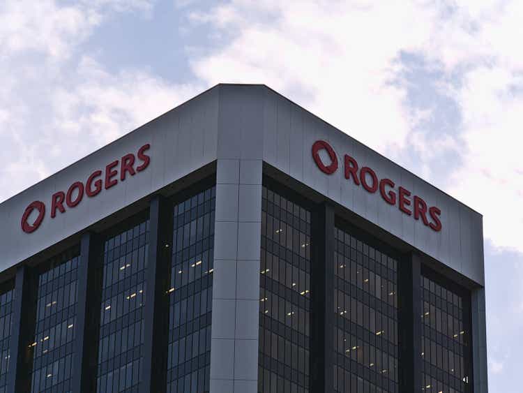 Low angle view of a modern office building with a glass facade and the corporate logo of Rogers Communications Inc. Above on a sunny fall day with clouds in the sky.