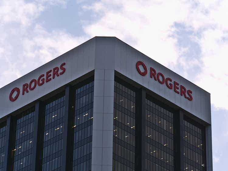 Low angle view of modern office building with glass facade and comapny logo of Rogers Communications Inc. on top on sunny day in autumn with clouds in the sky.