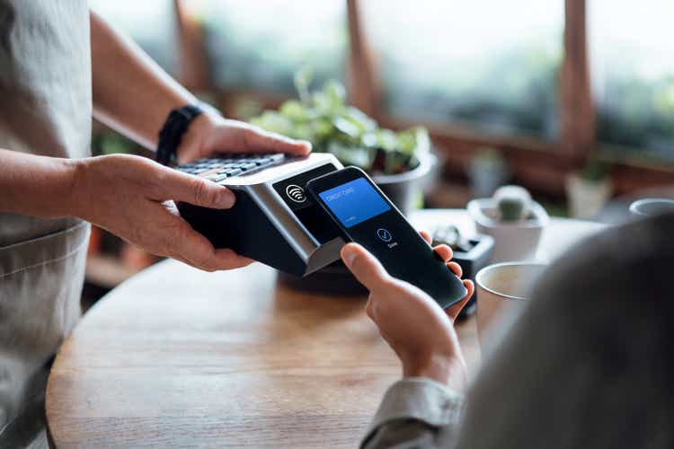 Close up of a male"s hand paying bill with credit card contactless payment on smartphone in a cafe, scanning on a card machine. Electronic payment. Banking and technology