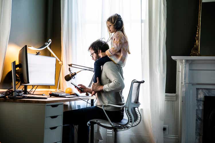 Father working in home office with young daughter on shoulders