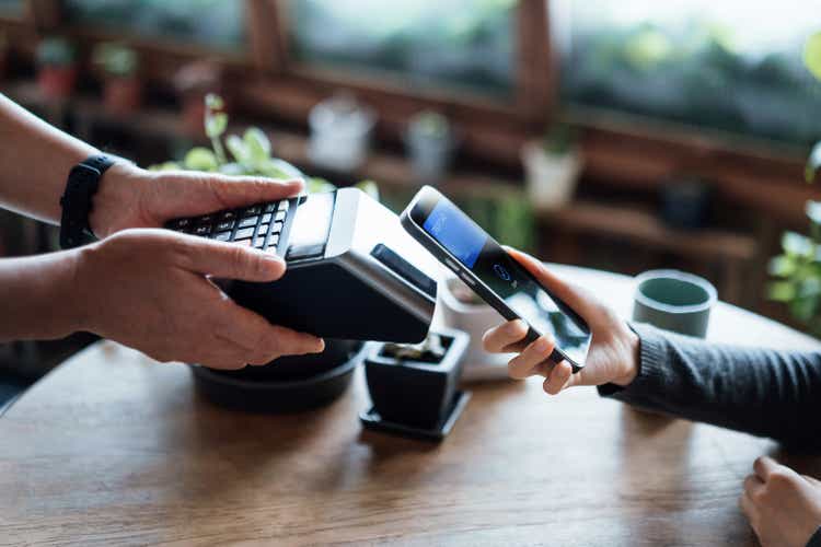 Close up of a woman"s hand paying bill with credit card contactless payment on smartphone in a cafe, scanning on a card machine. Electronic payment. Banking and technology