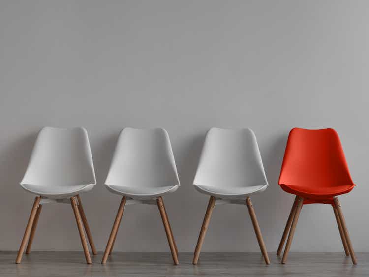 Drei leere weiße Stühle und einer rote auf grauem Wandhintergrund im Büro oder Raum