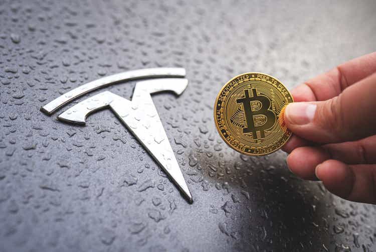 Person holds Bitcoin next to Tesla car