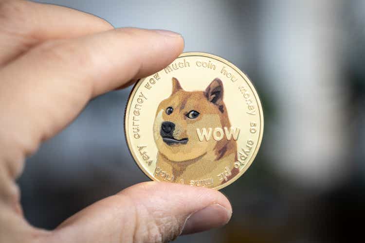 Dogecoin cryptocurrency physical coin held between two fingers.