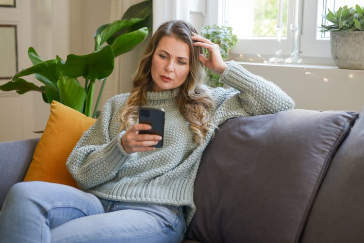 attractive middle aged woman sitting on the couch (negative emotions, smartphone))