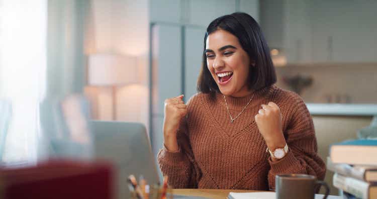 Shot of a young woman cheering while using a laptop to study at home