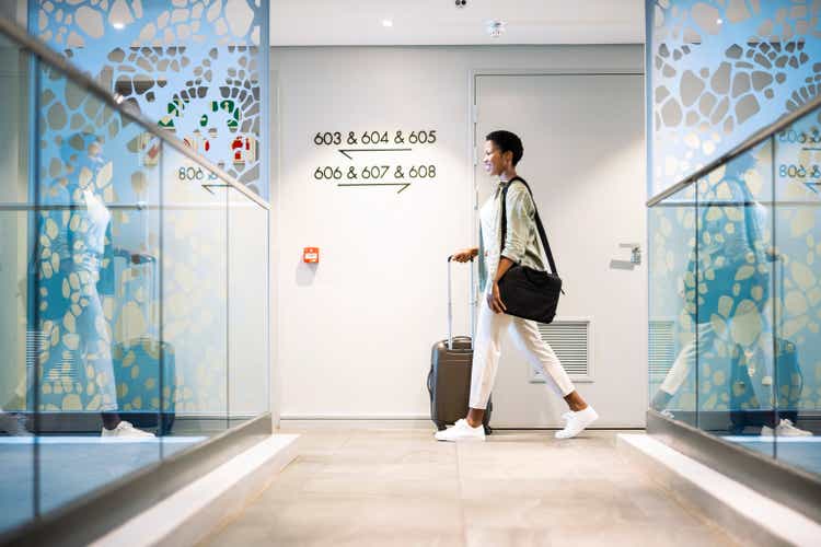 Young woman walking with wheeled luggage in hotel corridor