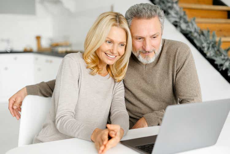 Verliebtes Paar mittleren Alters verbringt freizeitlich mit einem Laptop zu Hause