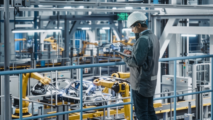 Multiethnic Car Factory Engineer in Work Uniform Using Tablet Computer. Automotive Industrial Manufacturing Facility Working on Vehicle Production with Robotic Arms. Automated Assembly Plant.