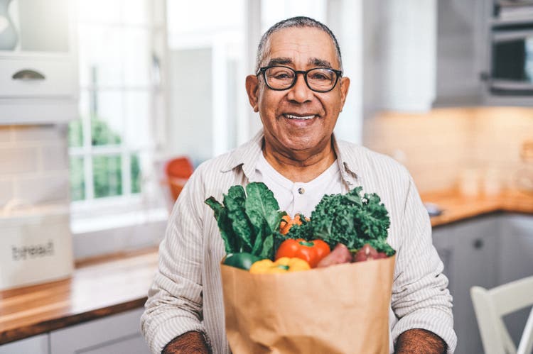 Shot of a elderly man holding a grocery bag in the kitchen