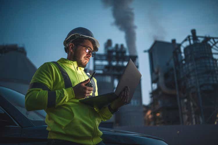 Concentrated engineer working with laptop during night shift in gas and oil industry station.