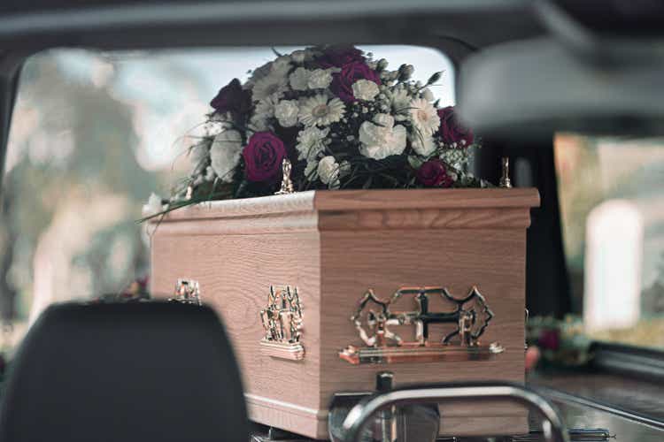 Flowers atop a coffin on display within a hearse at a funeral