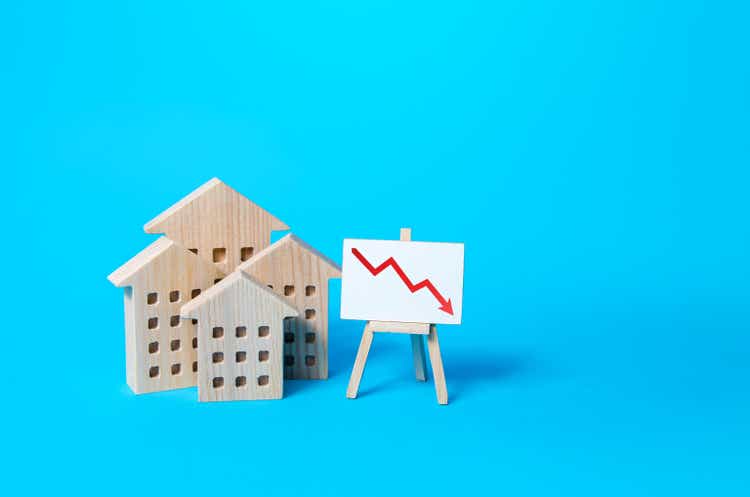 Residential buildings and down arrow graph on easel. Low property value, low price. Real estate market fall. Lower mortgage interest rates. Falling prices for rental. Affordable housing. Crisis