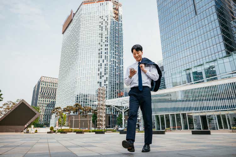 Mid adult Asian businessman in full suit in financial district, using smart phone