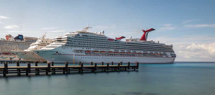 Low angle panoramic shot of Carnival Freedom docked in Cozumel. Gorgeous smooth turquoise water, wooden pier in the foreground. Blue sky in the background