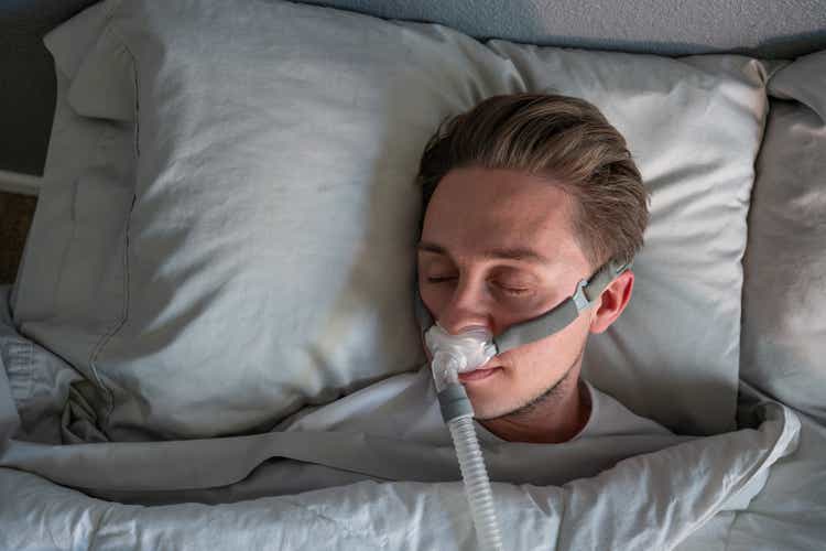 Close Up Of A Young Man With Sleep Apnea Wearing A CPAP Mask In Bed Sleeping On His Side