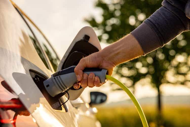 Man inserts a power cord into an electric car for charging in the nature