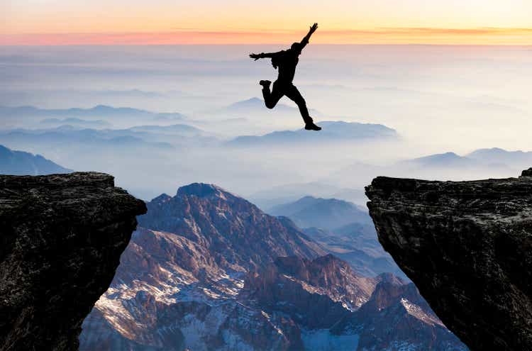 Silhouette of man jumping from one cliff to another cliff with excitement