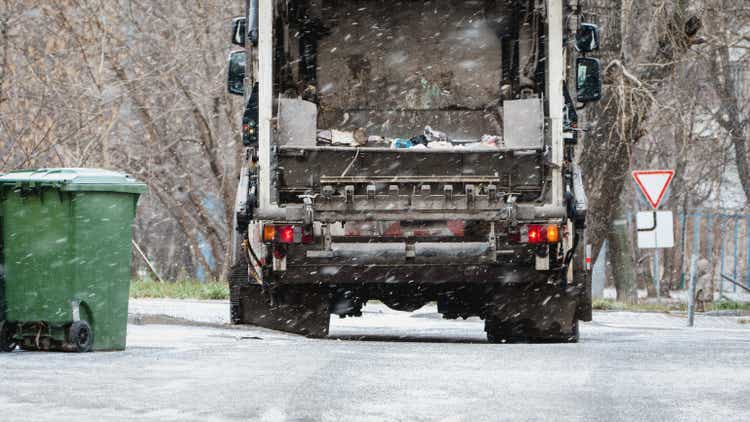 Garbage truck, dustcart with bin lift, household waste removal in residential area in winter, refuse container, snow