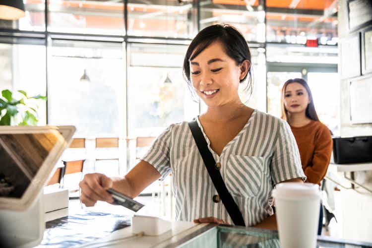 Young woman using credit card reader at coffee shop counter