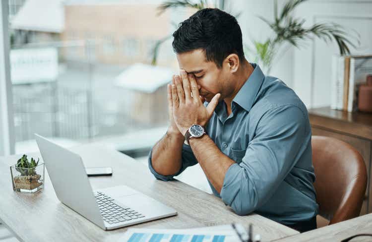 Shot of a young businessman looking stressed while working in a modern office