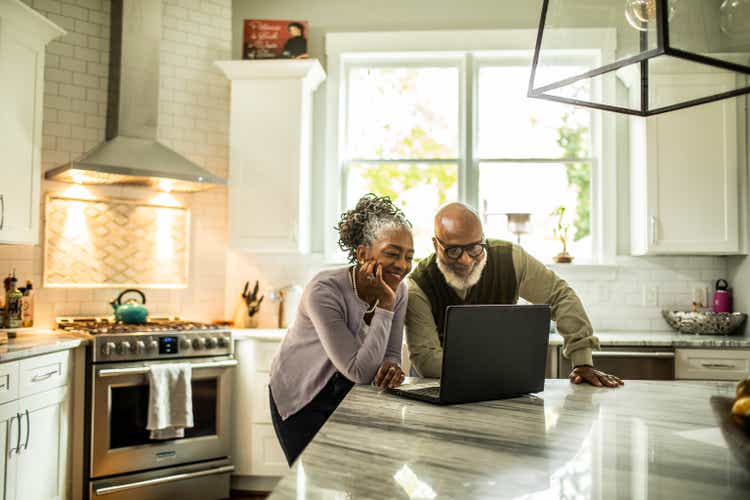 Senior couple using laptop in kitchen of suburban home