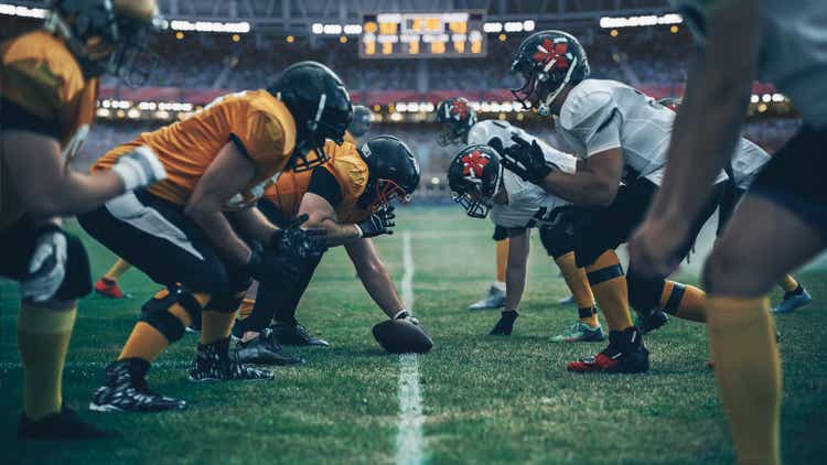 American Football Championship. Teams Ready: Professional Players, Aggressive Face-off, Ready for Pushing, Tackling. Competition Full of Brutal Energy, Power. Stadium Shot with Dramatic Light