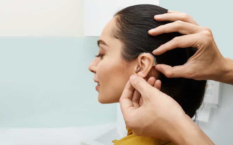 Installation hearing aid on woman"s ear at hearing clinic, close-up, side view. Deafness treatment, hearing solutions