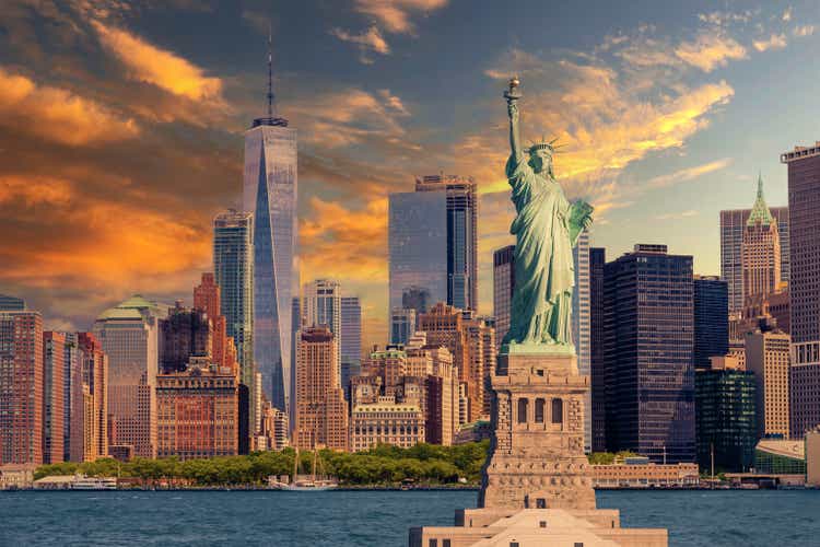 Statue of Liberty and New York City Skyline with Manhattan Financial District, World Trade Center and Orange and Blue Sunset Sky.