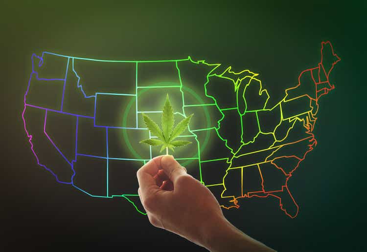 A female hand holds a cannabis leaf on a background of the USA map. Marijuana legalization concept.