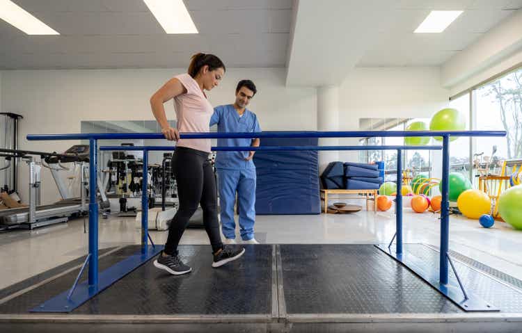 Woman during physical therapy walking on parallel bars