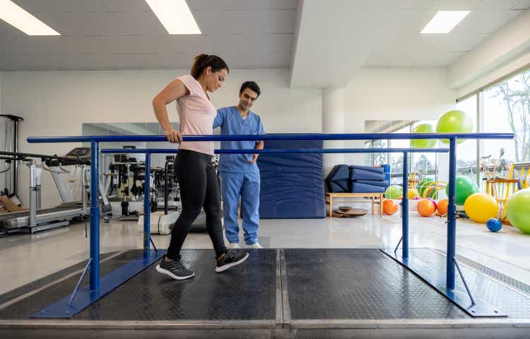 Woman in physical therapy walking on parallel bars.