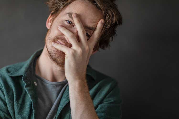 Young man looking at camera with hand covering face