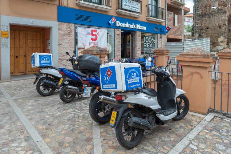 Several motorcycles for the delivery of pizzas parked next to the famous pizza chain Domino"s Pizza