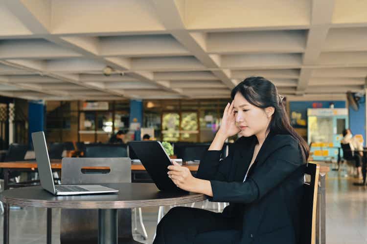 Stressed businesswoman sitting in office and using digital tablet.