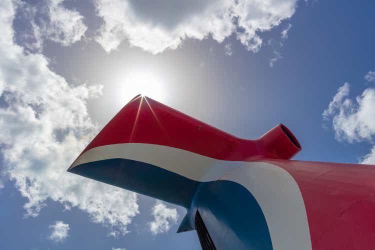 Belle photo à angle bas de l’entonnoir rouge, blanc et bleu sur Carnival Freedom. Les rayons du soleil et le soleil brillent et le ciel bleu avec des nuages blancs en arrière-plan