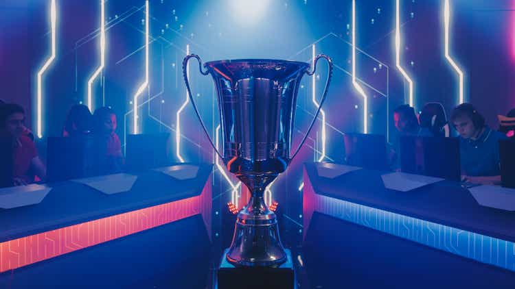 Two Esport Teams of Pro Gamers Play to Compete in Video Game on a Championship. Stylish Neon Cyber Games Online Streaming Tournament Arena with Trophy in the Center.