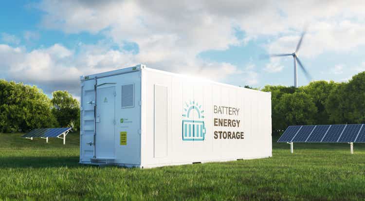 A concept of a modern high-capacity battery energy storage system in a container in the middle of a green field with a forest in the background.  3D rendering