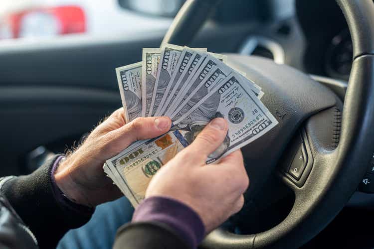 hands holding dollar bills in the middle in the car interior on the steering wheel background