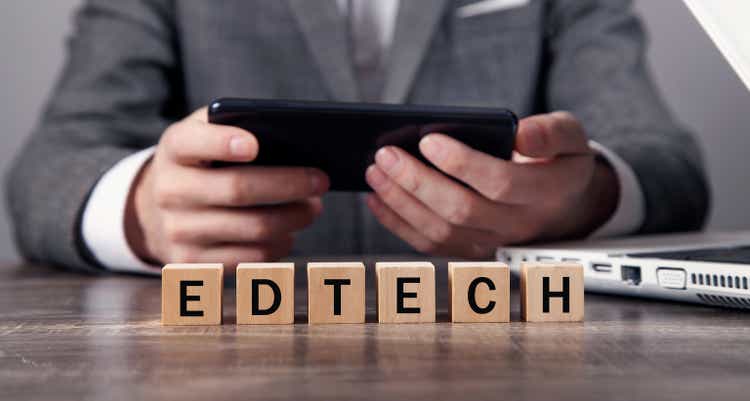 Man using smartphone with a word EdTech on wooden cubes.