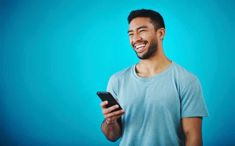 Shot of a handsome young man holding a cellphone while standing against a blue background