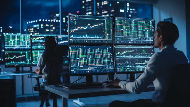 Financial Analyst Work on a desktop with a multi-screen workstation with real-time stocks, commodities and forex charts.  Businessman working at Investment Bank City Office at night.