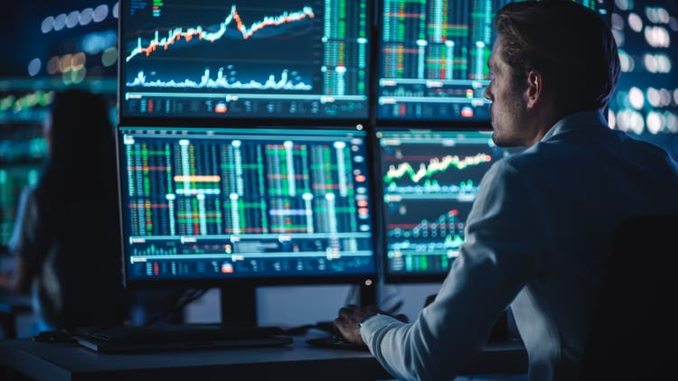 Financial Analyst Working on a Computer with Multi-Monitor Workstation with Real-Time Stocks, Commodities and Foreign Exchange Charts. Businessman Works in Investment Bank City Office at Night.