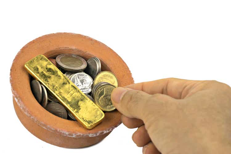 Hand pick up money, put the cup clay.(in the clay cup with lots of silver and gold) isolated on white background.